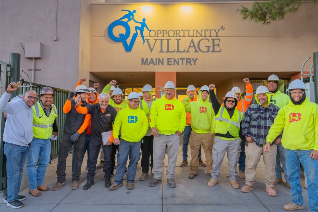 Some Hirschi workers along with others are standing in front of Opportunity Village main entry, smiling for the camera.